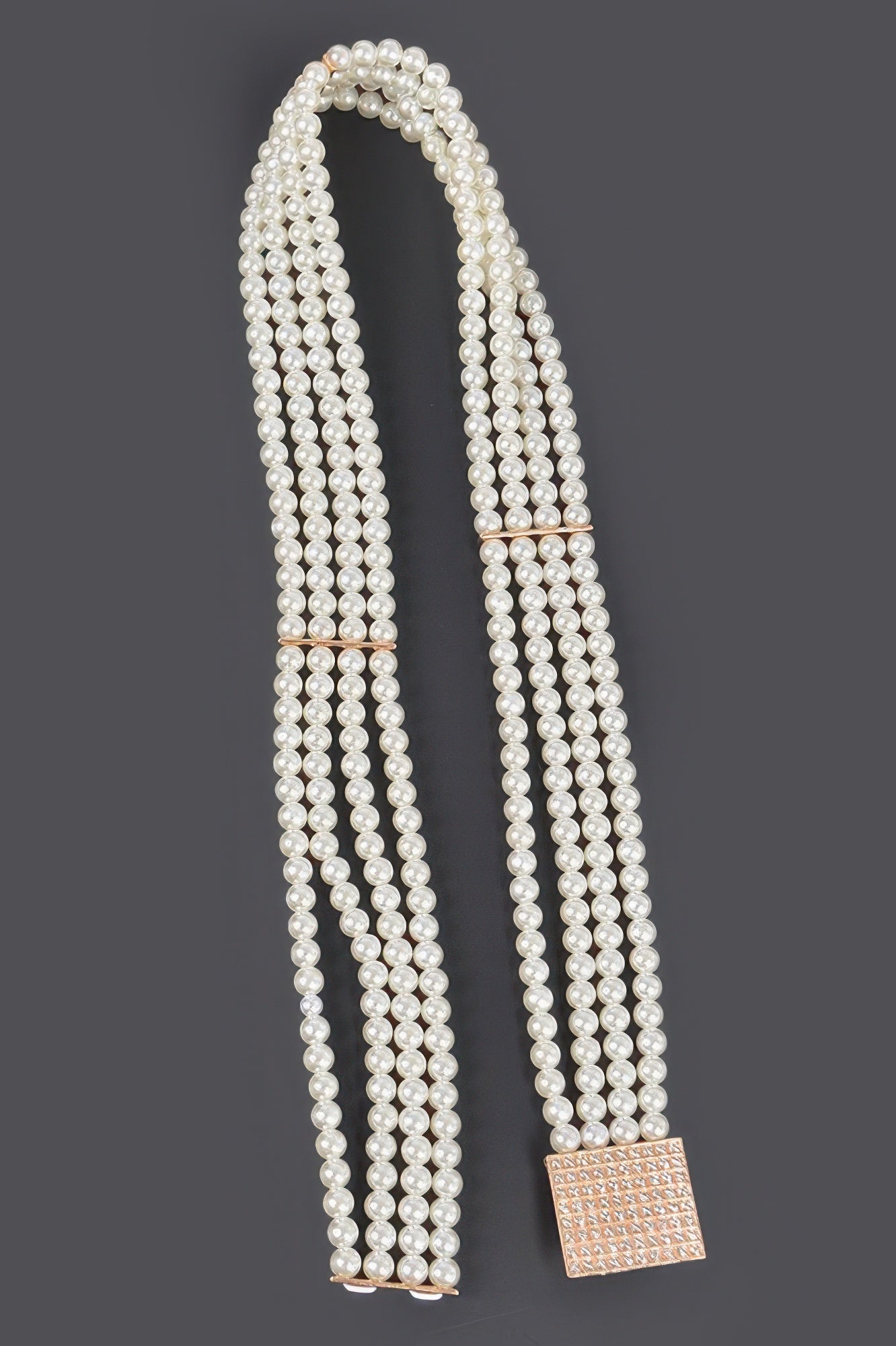 Ivory pearl elastic belt laid out, with square rose-gold buckle and hanging ends