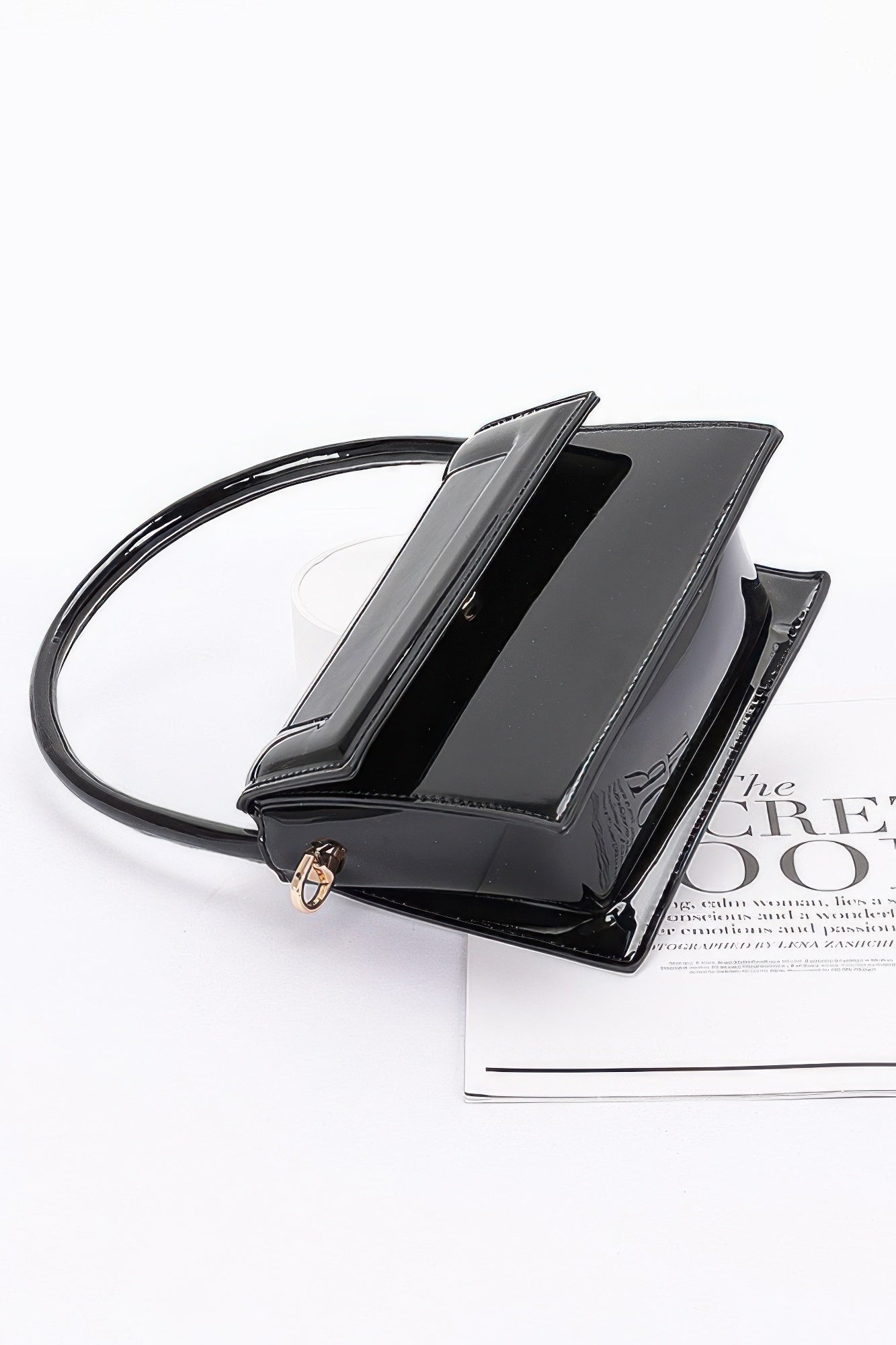 Enamel top handle flap bag, black angled view showing flap and front clasp