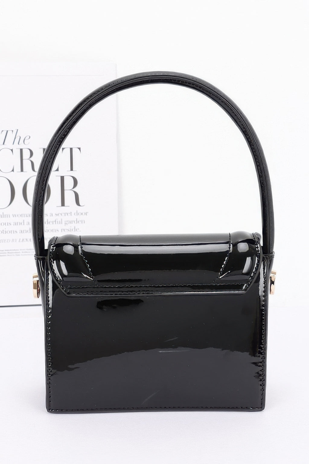 Enamel top handle flap bag, black front view with patent-like sheen and flap