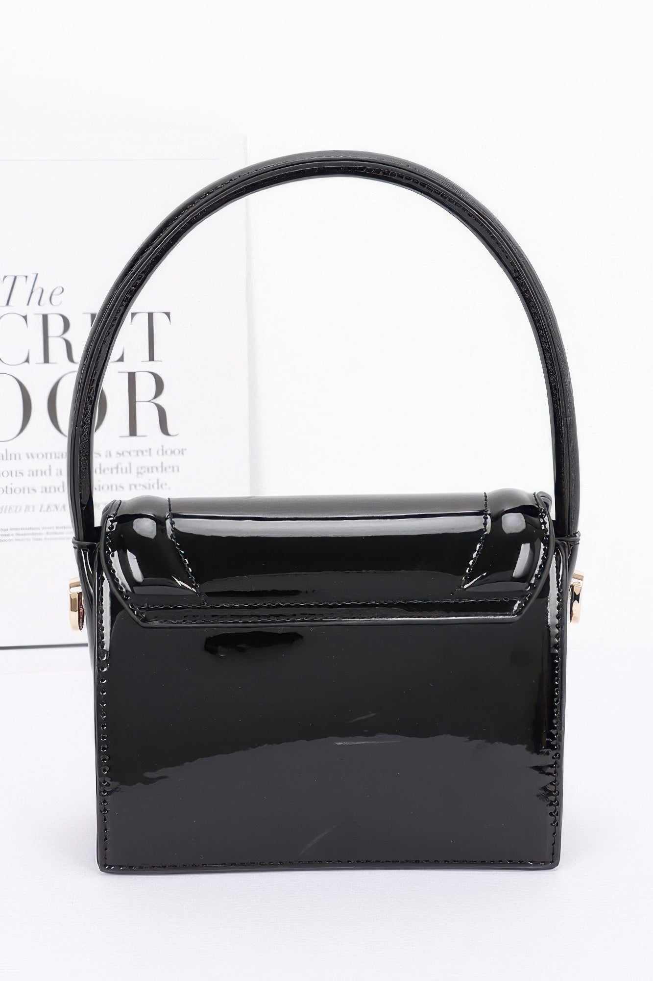 Enamel top handle flap bag, black front view with patent-like sheen and flap