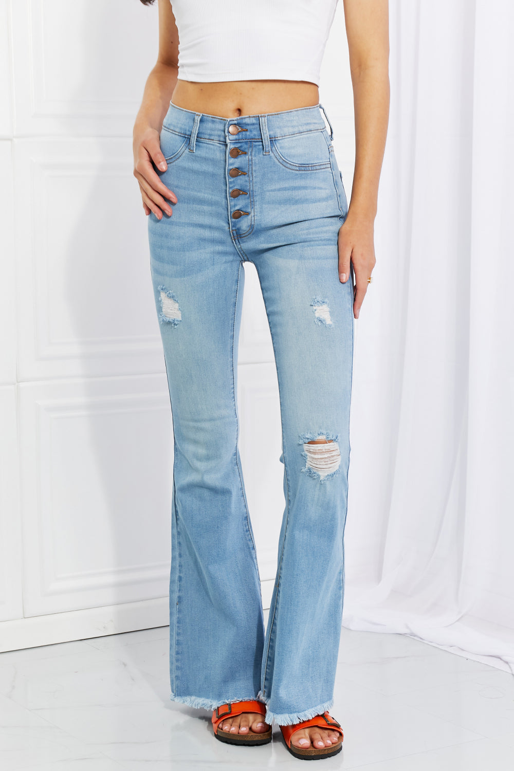 Light blue flare jeans with button front, ripped patches, and frayed ankle hem