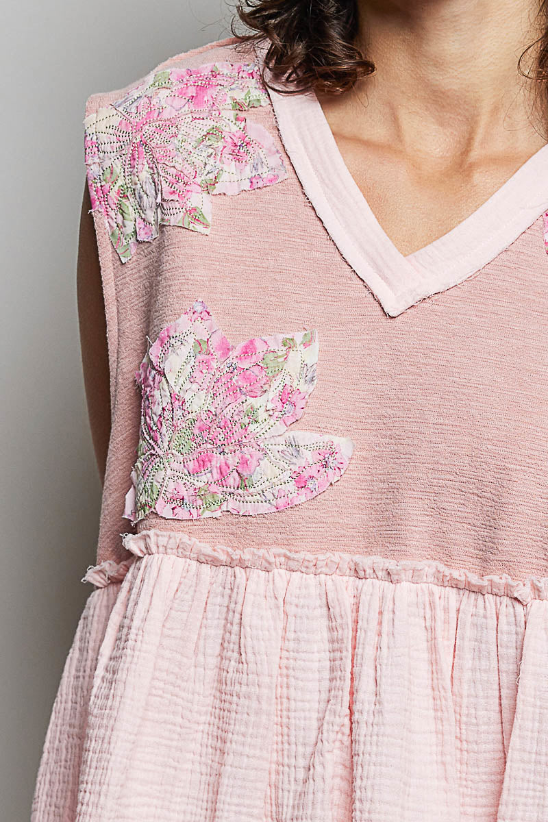 Close-up: powder pink V-neck sleeveless top with floral patch and raw-edge ruffles