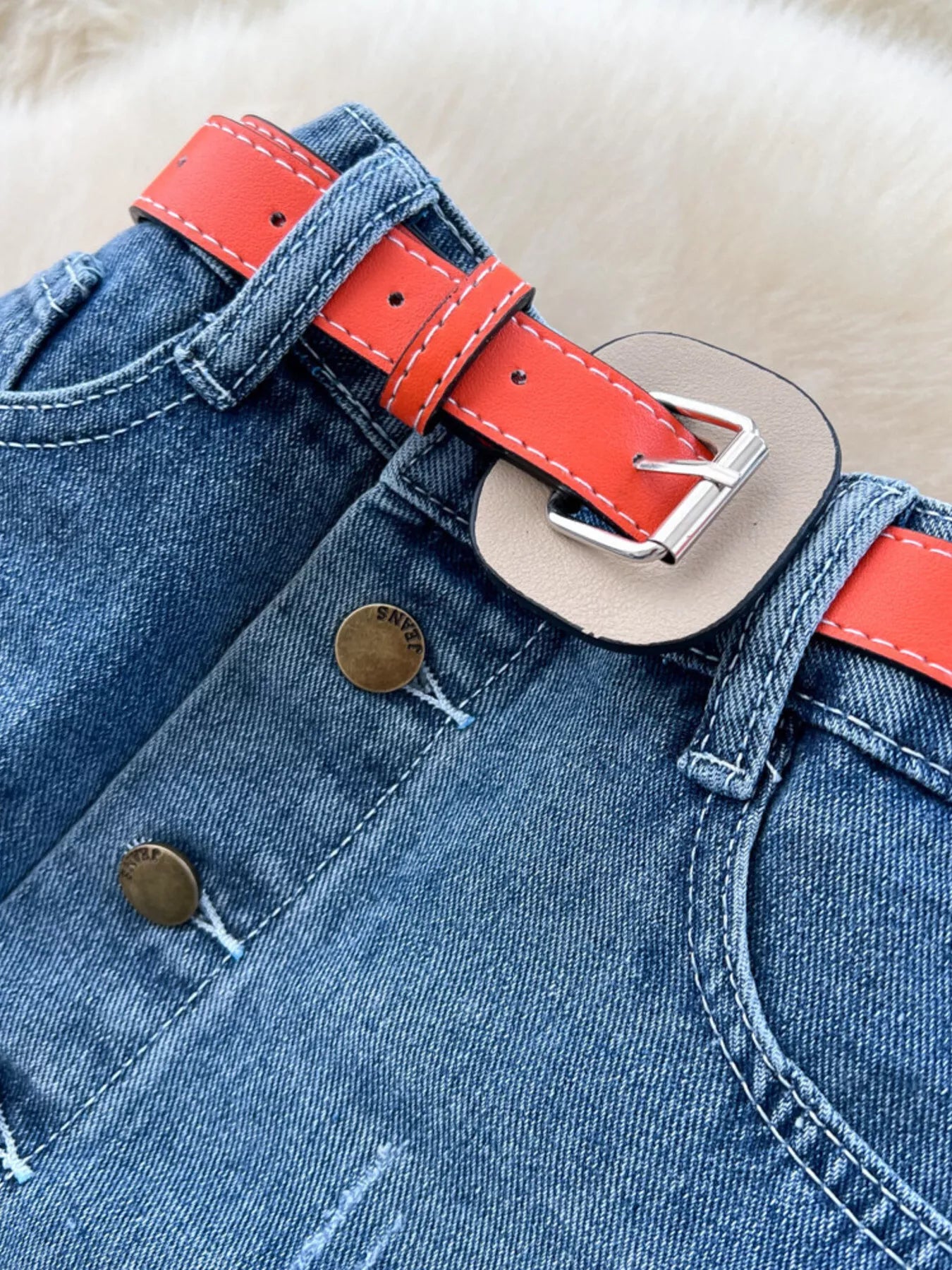 Cintura con cinturón rojo y hebilla plateada; botones dorados y trabilla en denim