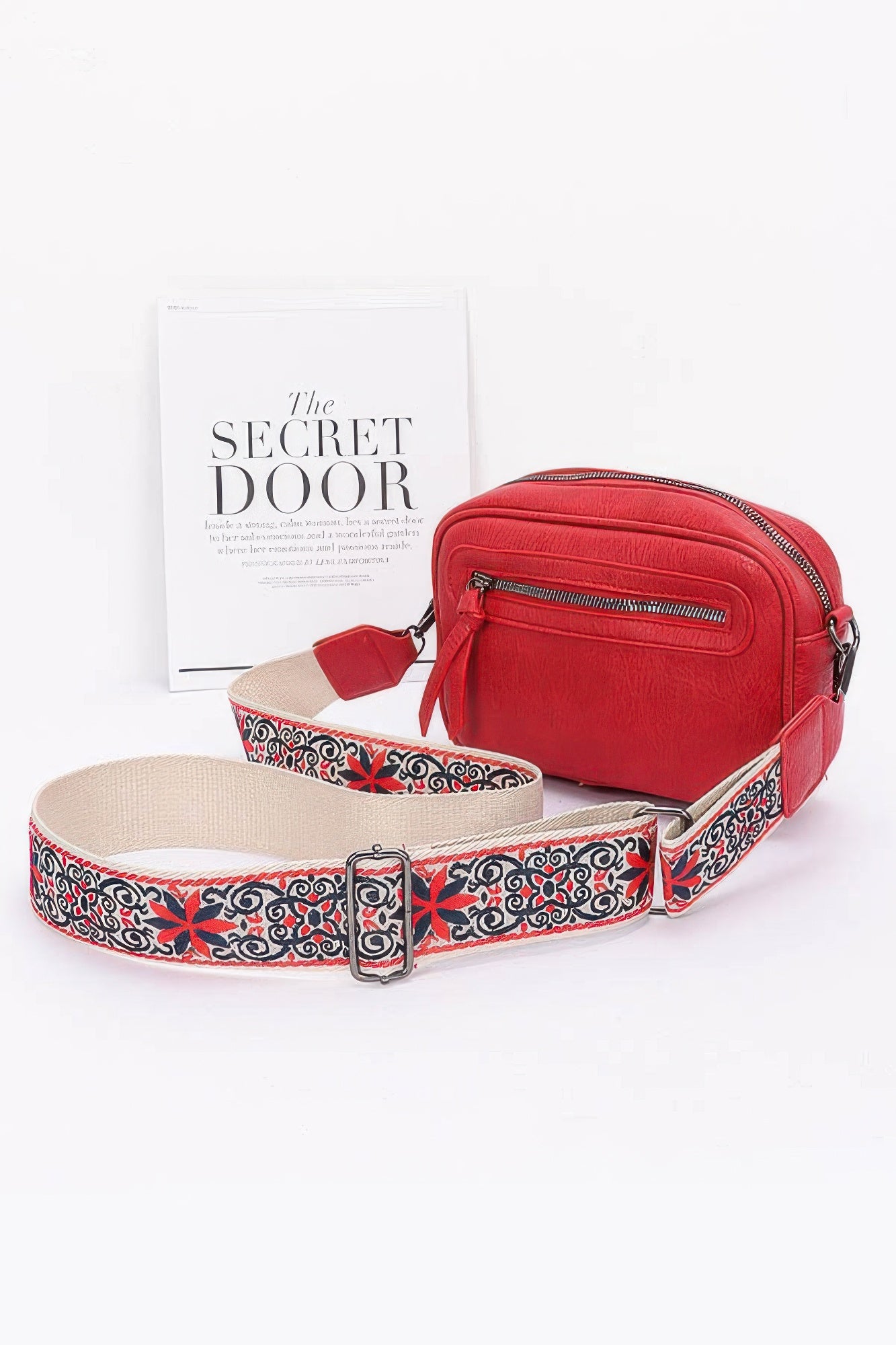 Red faux leather camera bag with front zip pocket and multicolor patterned strap