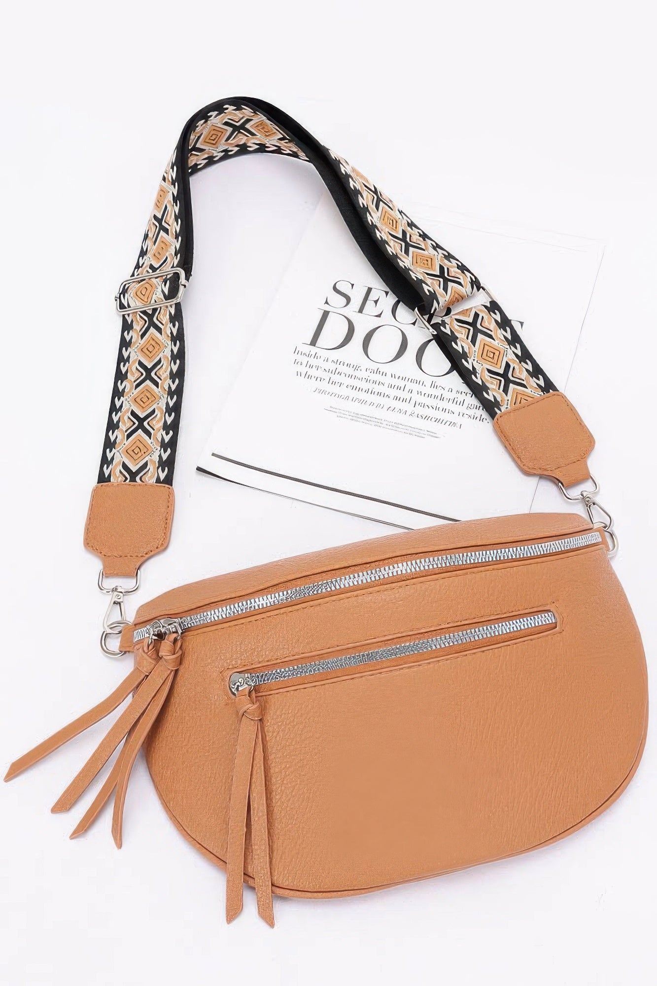 Tan faux leather crossbody bag with patterned strap, two front zippers, tassel pulls.