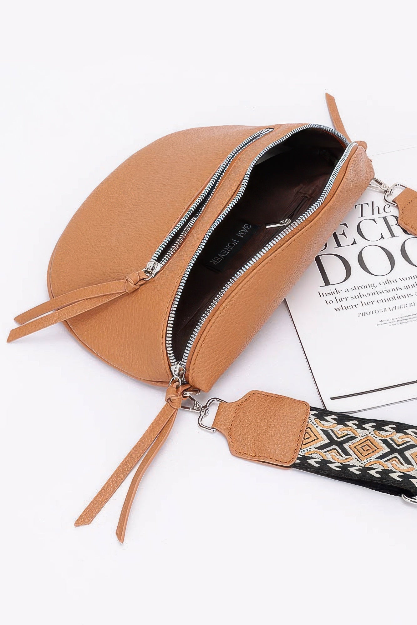 Camel crossbody bag open to show dark interior and front zip pocket; key clip charm.