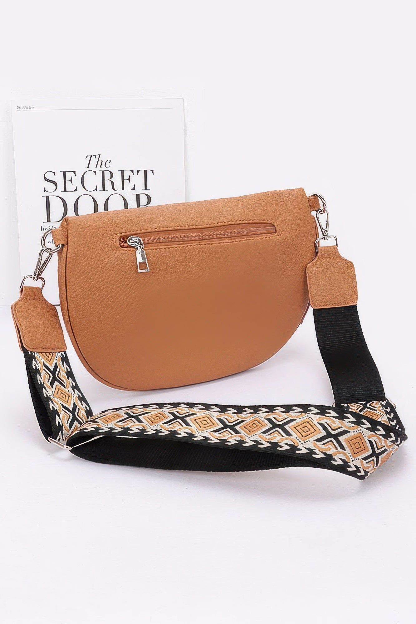 Camel half-moon crossbody bag with top zip, front zip pocket, and patterned shoulder strap.