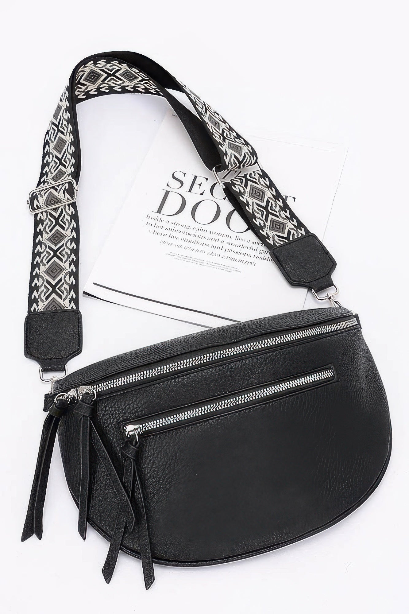 Black faux leather crossbody bag with patterned strap, dual zippers, and hanging tassels.