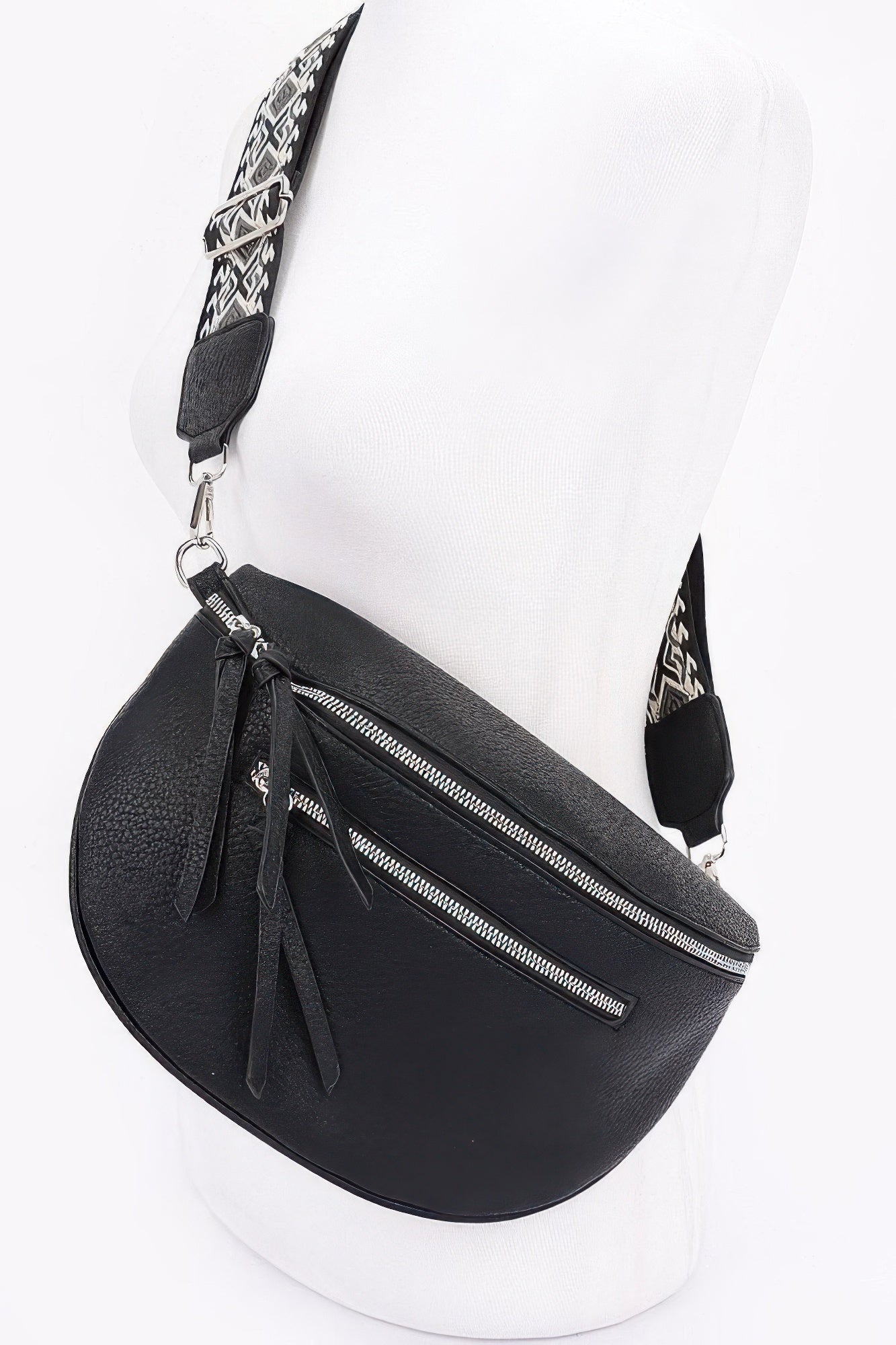 Black crossbody bag with front zip pocket, tassel charm, and patterned strap detail.