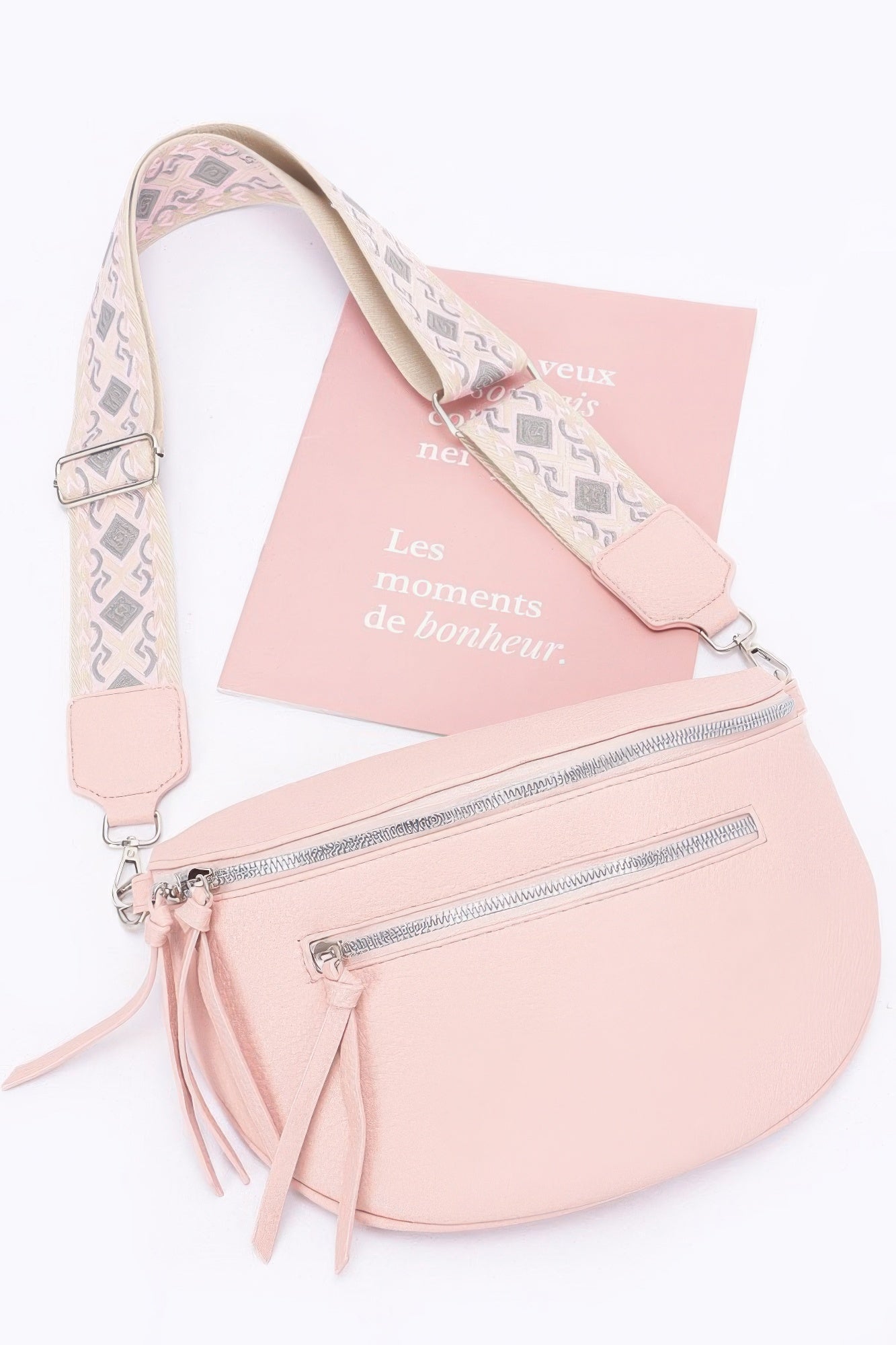 Pink faux leather crossbody bag with patterned strap, dual zippers, and fringe tassels.