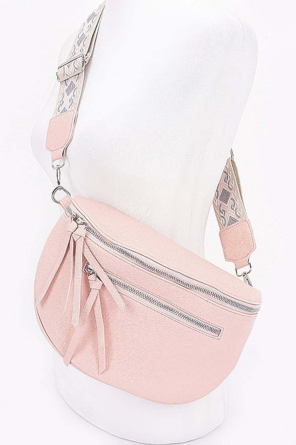 Light pink half-moon crossbody bag with front zipper and tassel fringe; patterned strap.