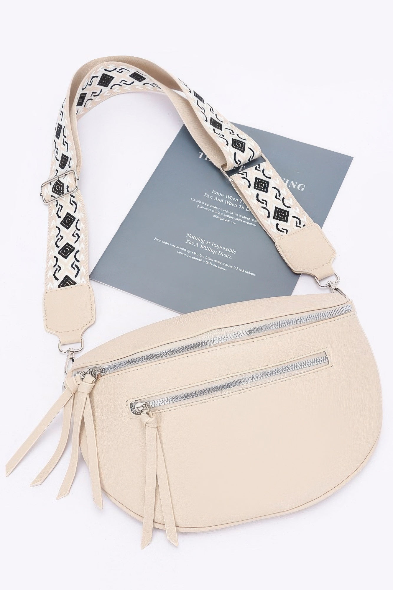 Beige faux leather crossbody bag with patterned strap, front zip pocket, and tassels.