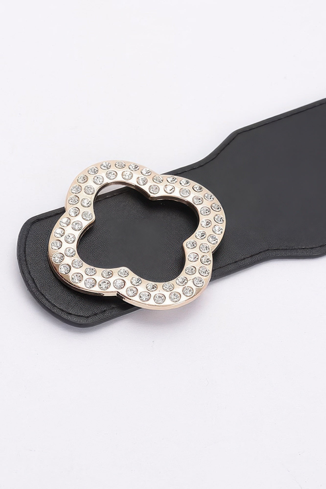 Close-up: black faux leather belt with rhinestone clover buckle, silver edge