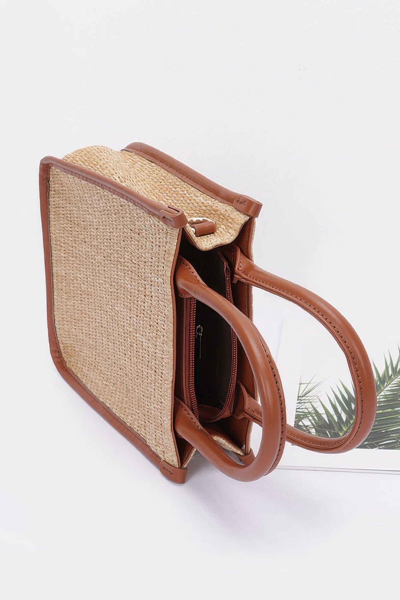 Side view of khaki faux straw tote bag with open interior and tan leather handles