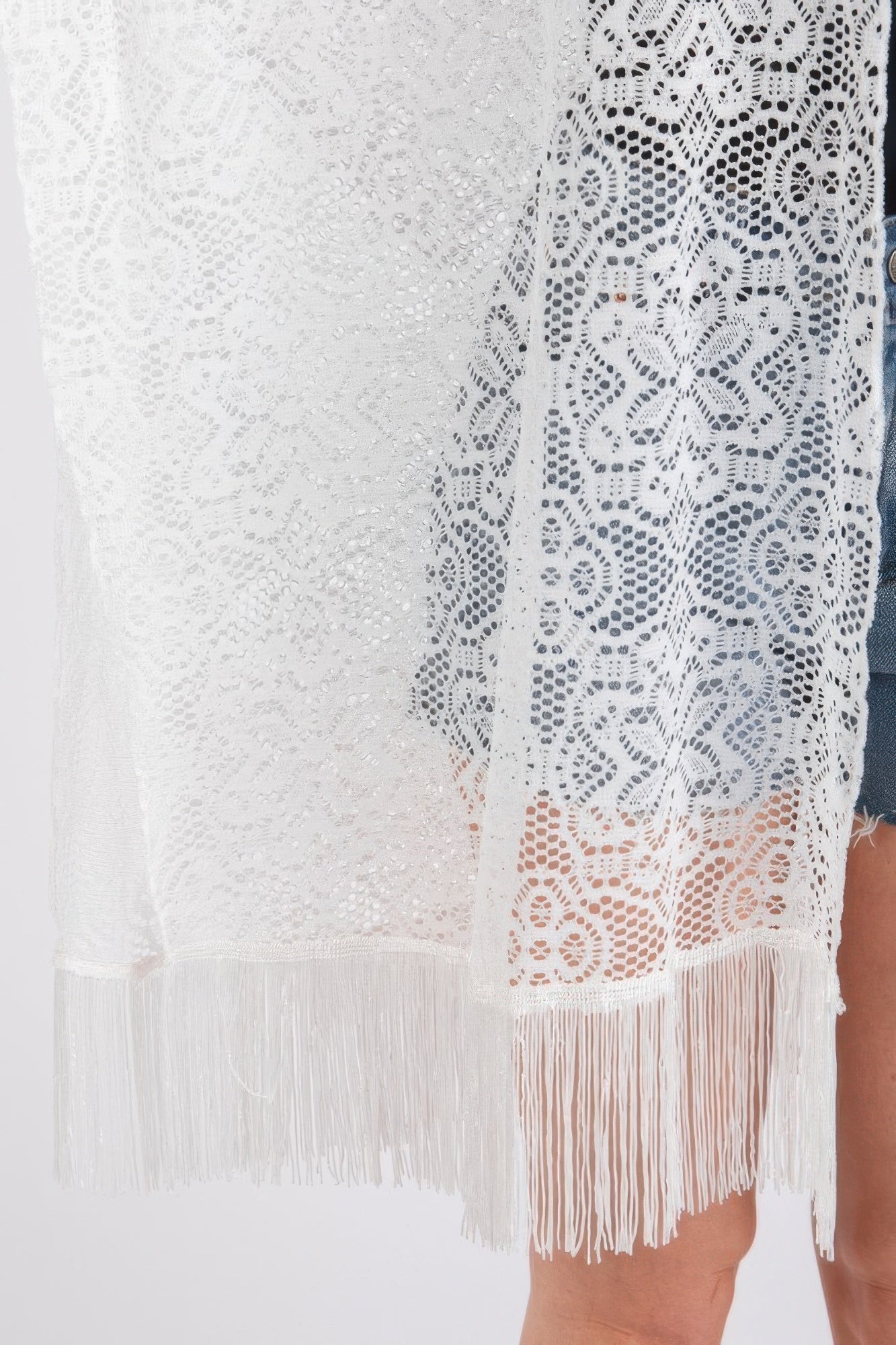Detail view of white crochet lace cover up with floral pattern and tassel trim
