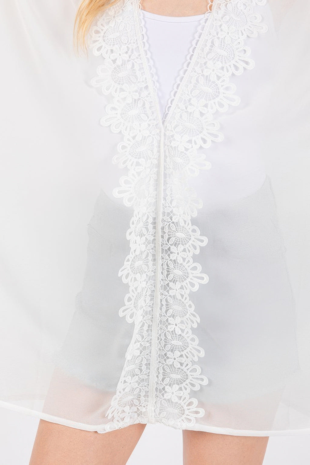 Close-up of white poncho: floral lace trim along center placket and hem
