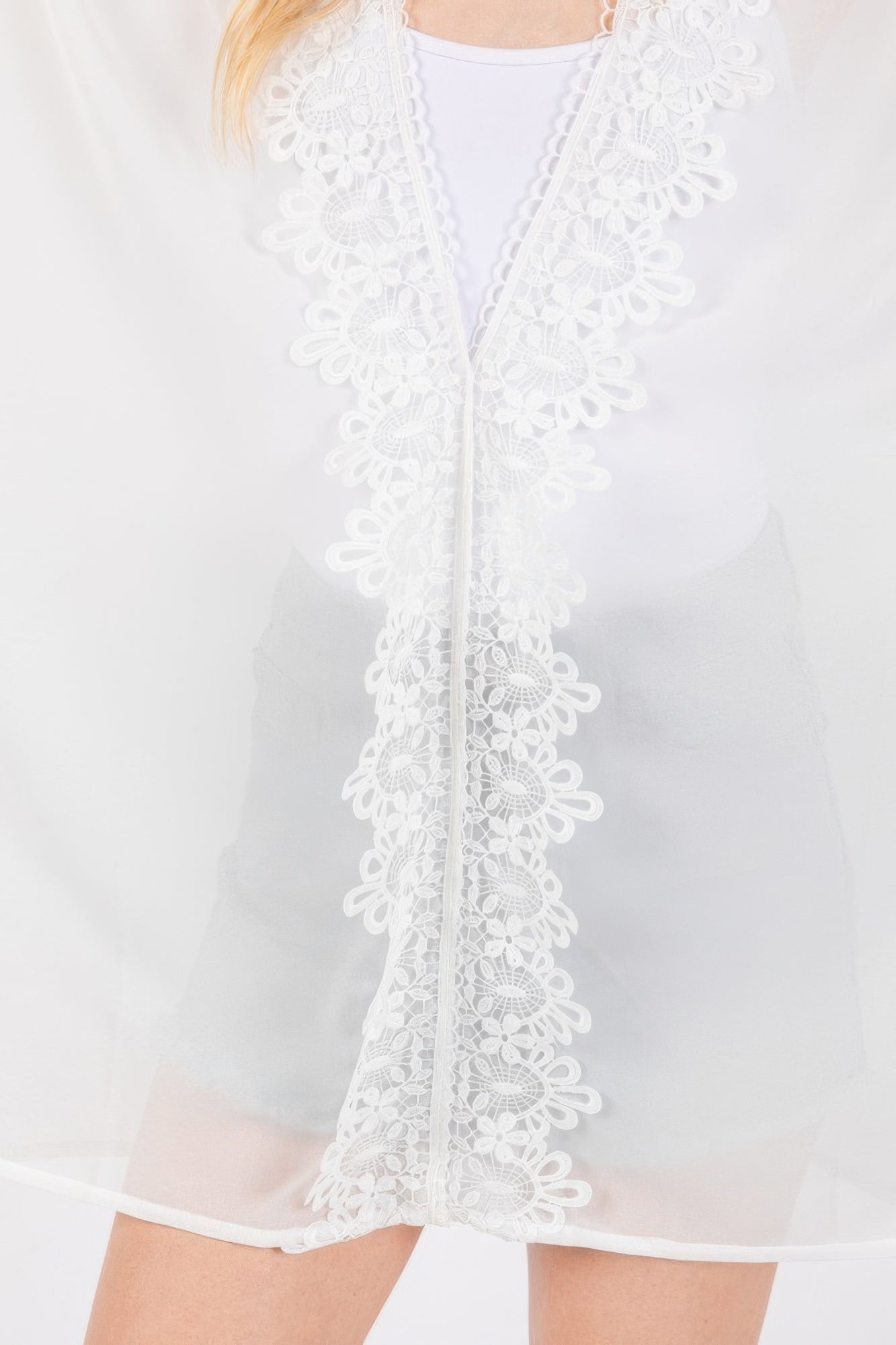 Close-up of white poncho: floral lace trim along center placket and hem