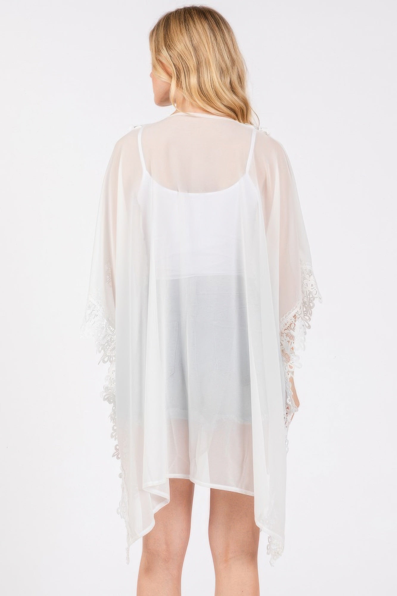 Back view of white flower-trim poncho with sheer overlay and lace sleeve details