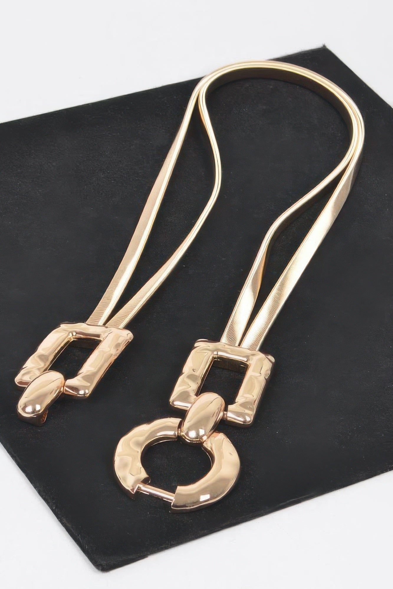 Gold metal buckle belt with O-ring center and two rectangular plates, laid flat