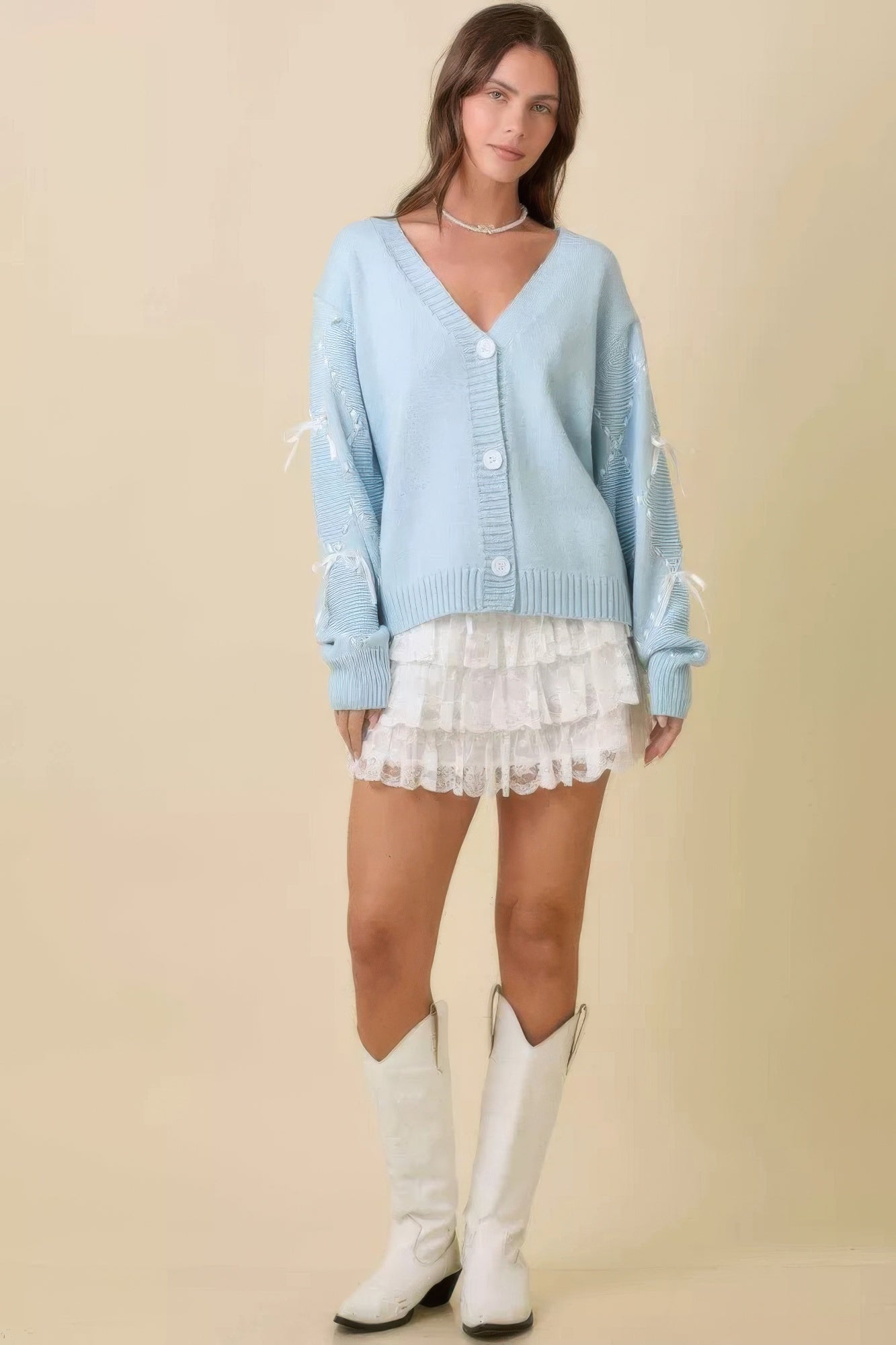 Cardigan azul claro con botones al frente, bajo de volante blanco y mangas con lazos