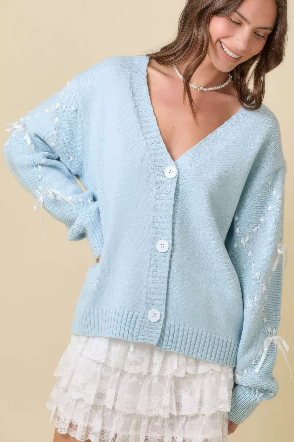 Cardigan azul claro con botones al frente y bajo de volante blanco; mangas decoradas