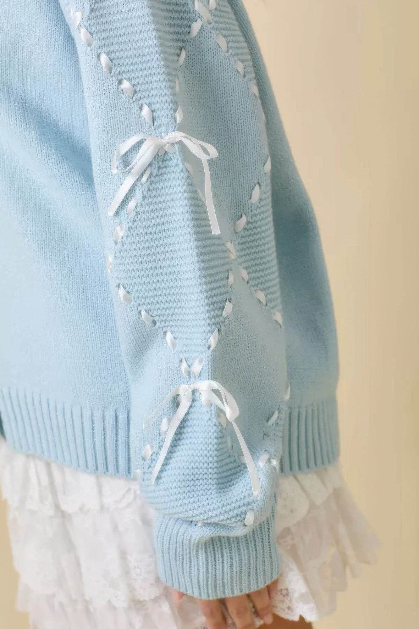 Detalle de mangas del cardigan azul claro: bordado con lazos blancos en la parte superior