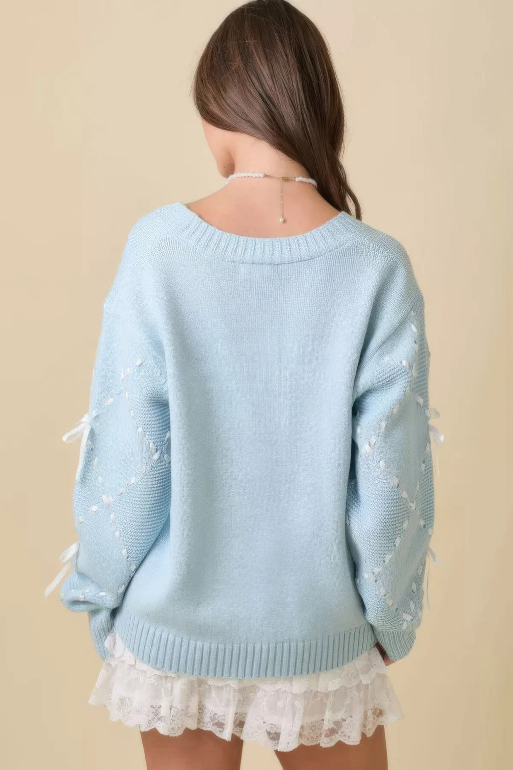 Vista trasera del cardigan azul claro con mangas decoradas con lazos y bajo volante blanco