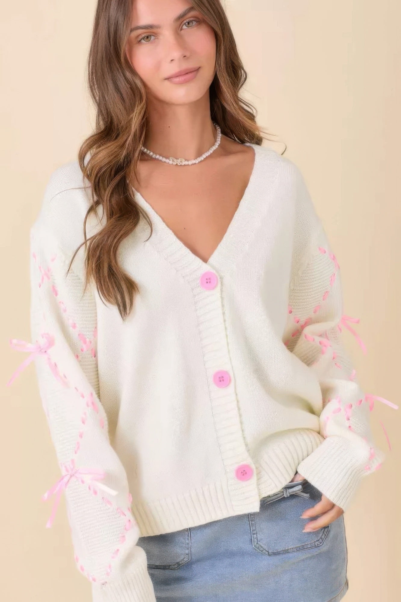 Cardigan crema con botones al frente y mangas con lazos rosados tipo satén