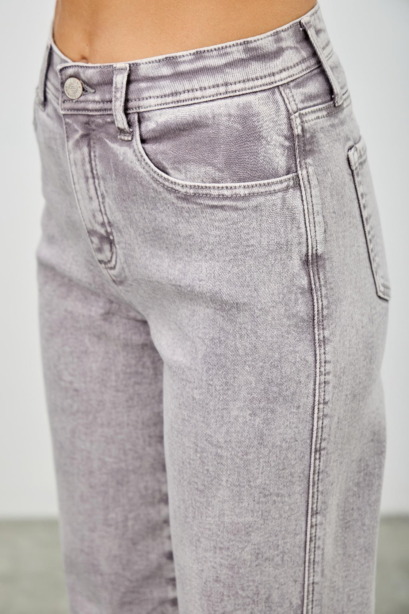 Close-up: light gray high rise denim jeans with belt loops, button fly, and back yoke.