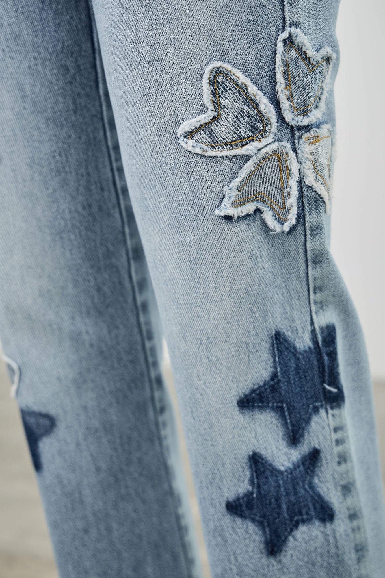 Close-up: stitched star patches on light-wash denim with a ripped-texture look