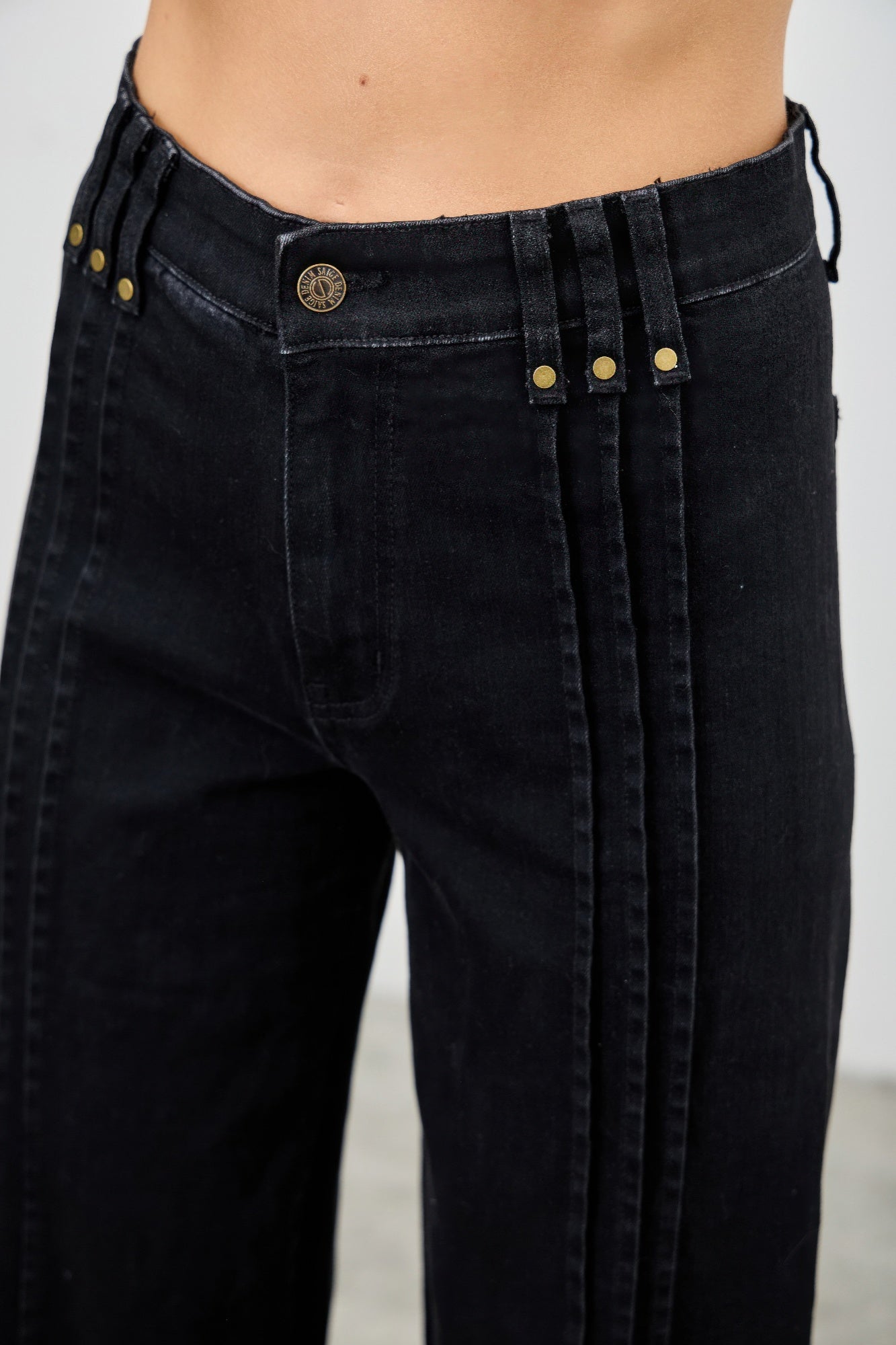 Close-up of high-rise black jeans front: round logo button and vertical seam stripes