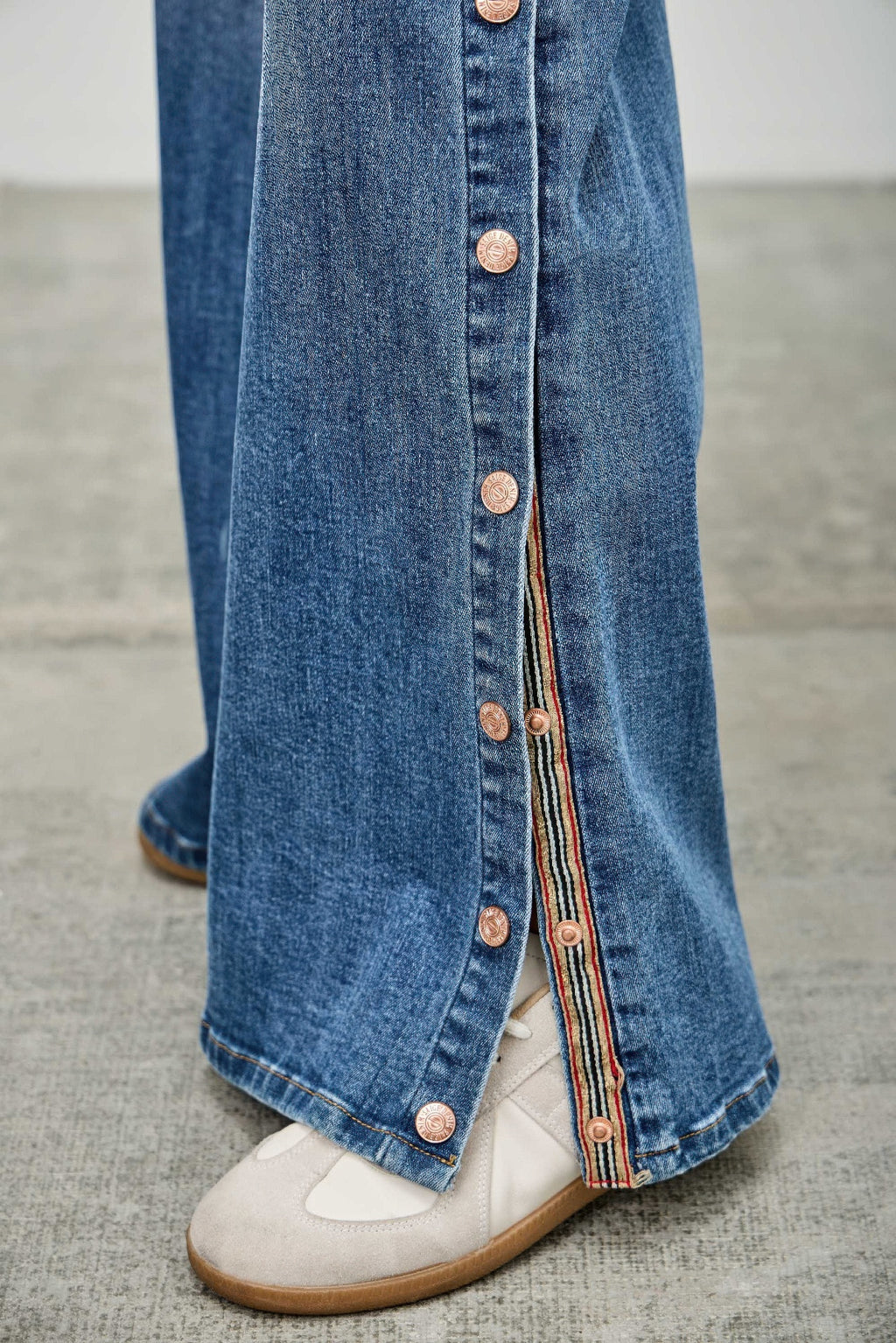 Blue denim wide-leg jeans with vertical snap buttons on the outer seam
