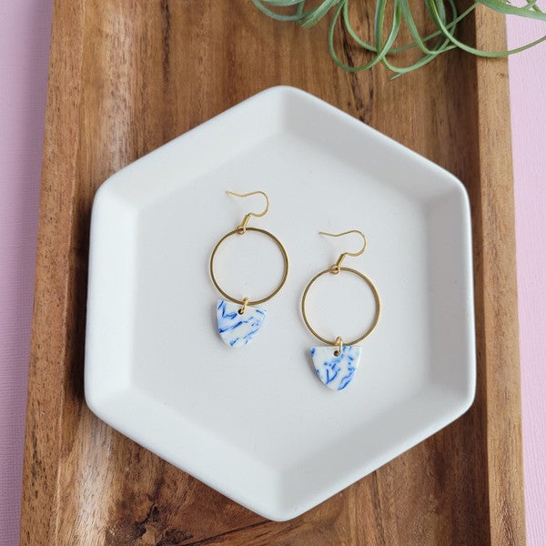 Gold hoop earrings with blue patterned drops on a white tray