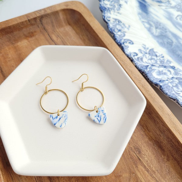 Gold hoop earrings with blue patterned drops, side-by-side on tray