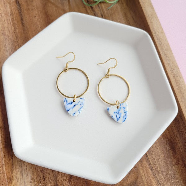 Pair of gold hoop earrings with blue patterned drops on white tray