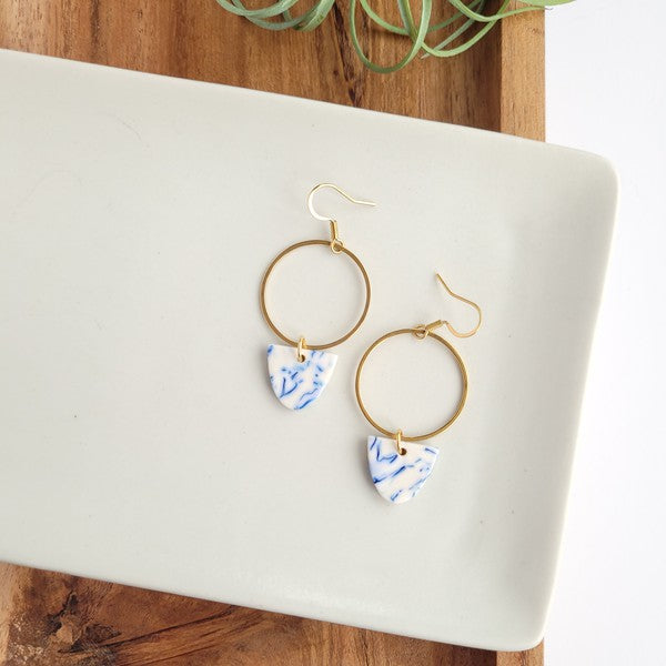 Close view of gold hoop earrings with blue patterned drops on tray