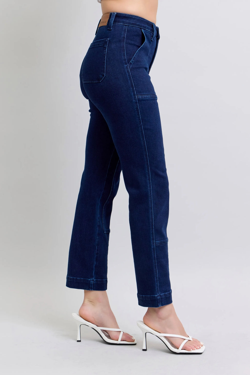 Dark blue straight jeans, side view with knee patch seams and back yoke.