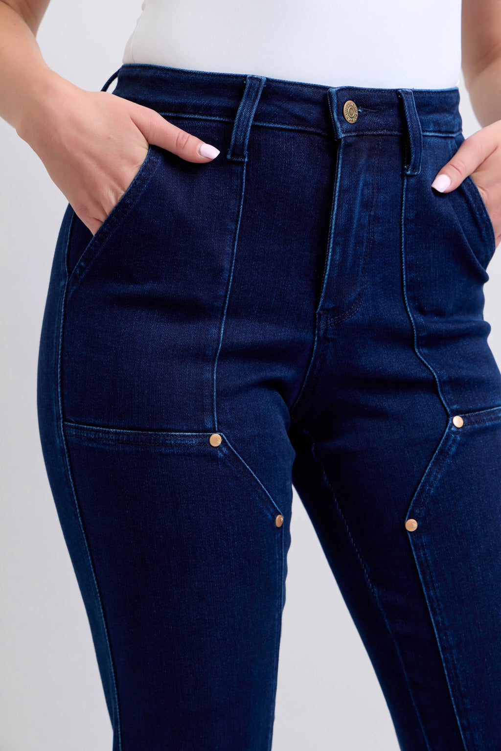 Dark blue denim waistband close-up with button, belt loops, knee patch pockets.