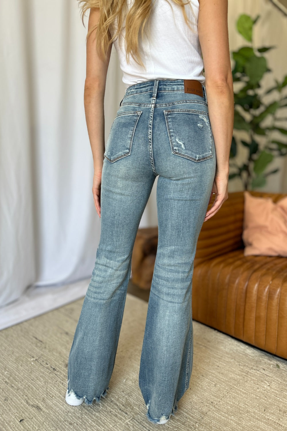Back view of medium wash flare jeans with distressed knees and frayed ankle hems