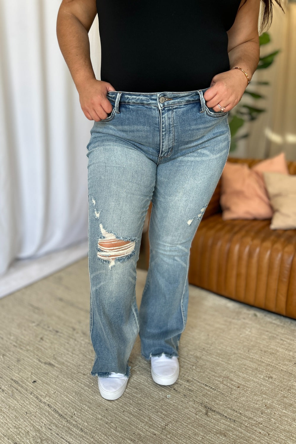Light-wash flare jeans, mid-rise waist with large raw knee tear and frayed hem