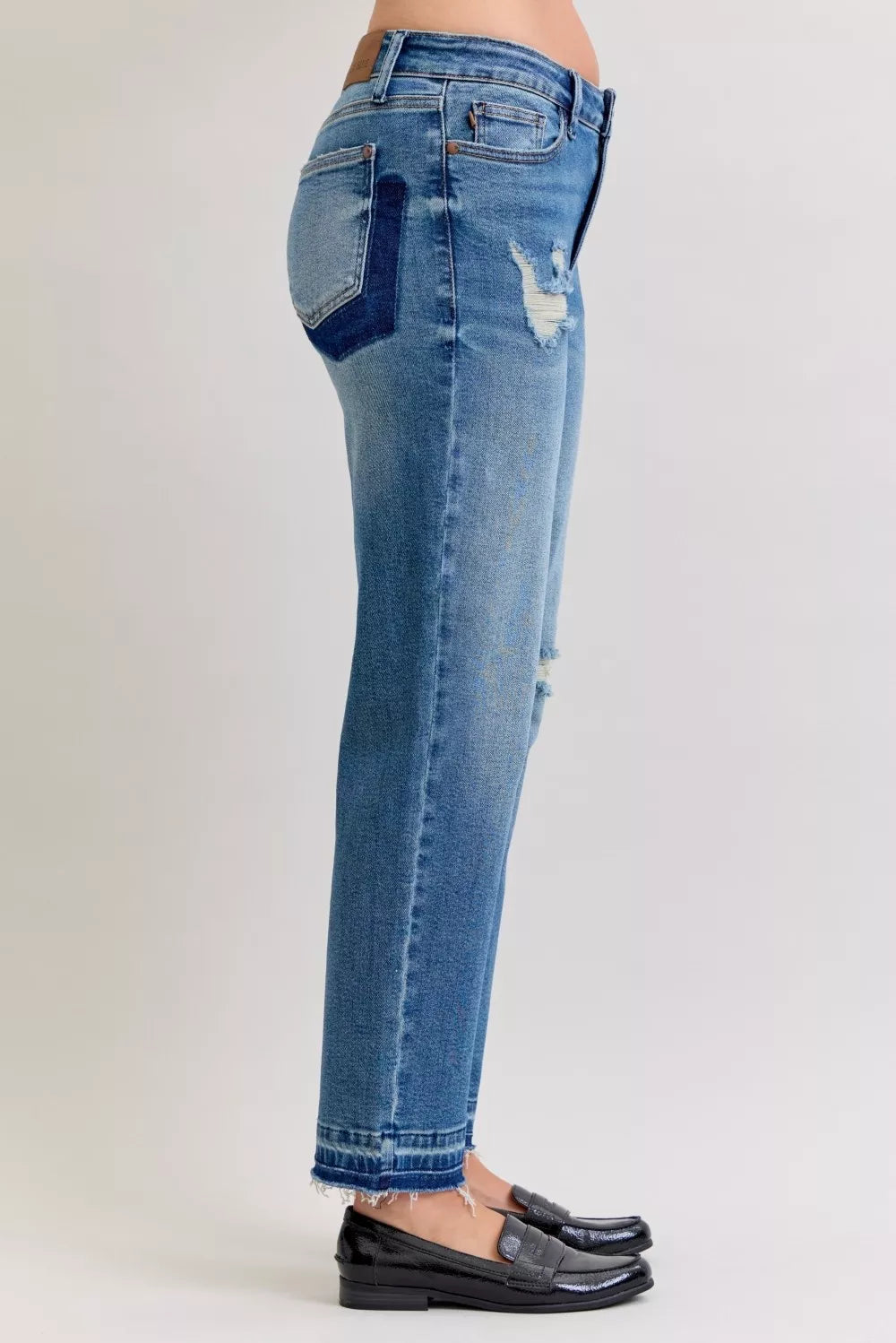Back view: medium blue mid-rise jeans with repair patches and frayed release hem
