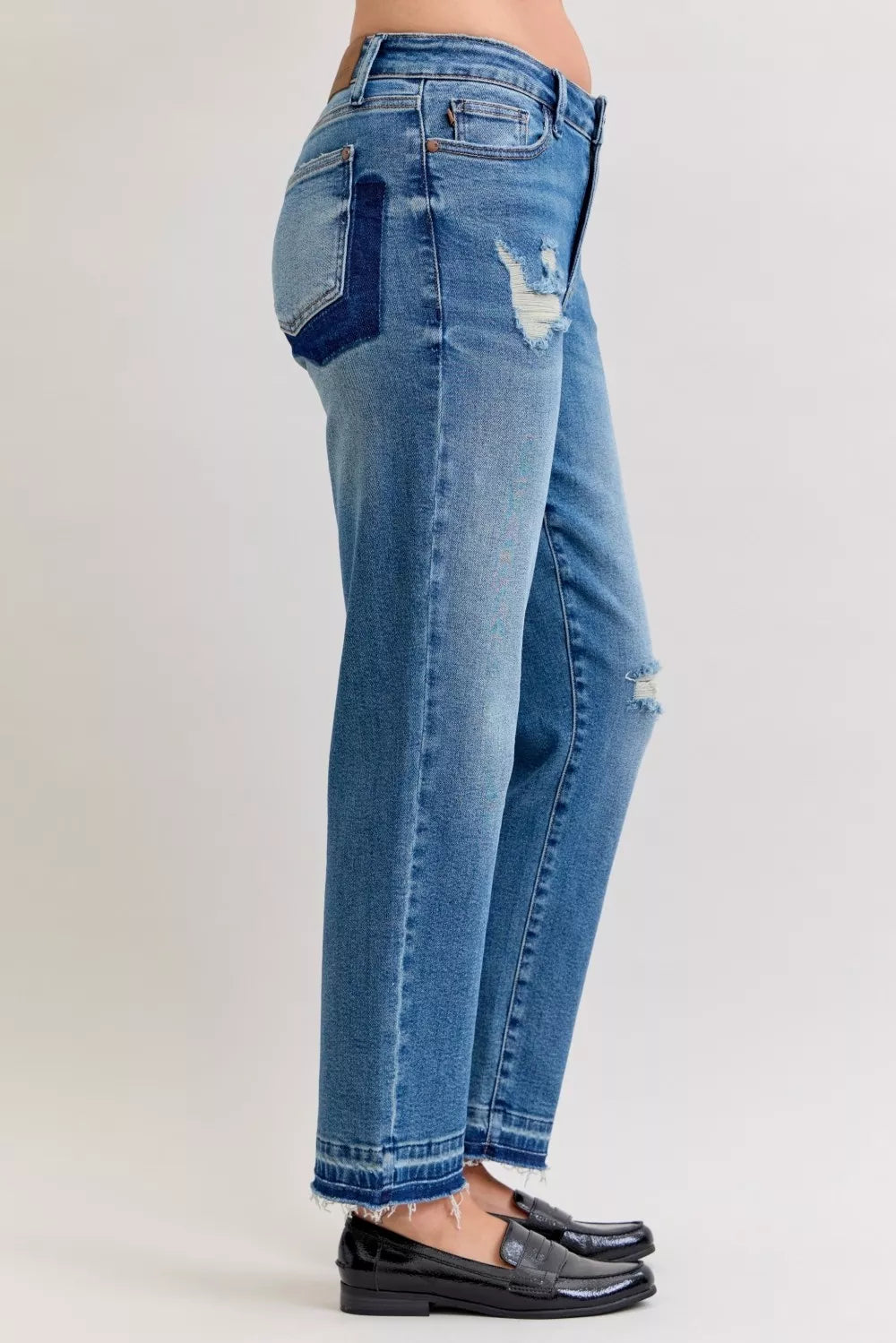 Back view of medium blue mid-rise jeans with side repair patches and raw hem