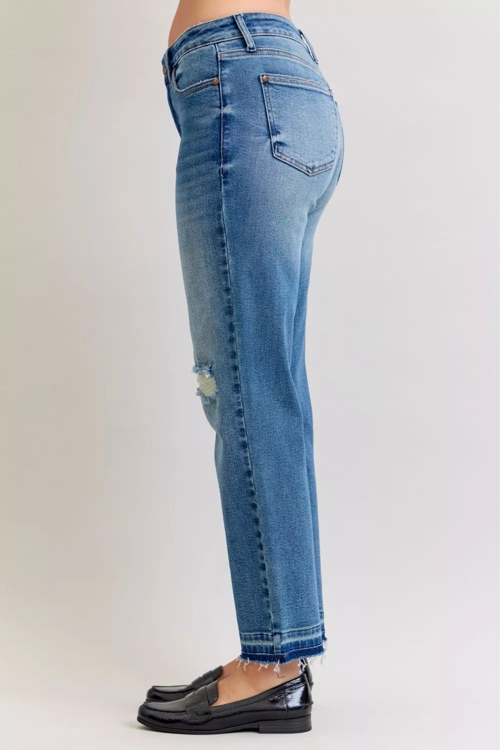 Side view of medium blue mid-rise jeans with front repair patch and frayed ankle hem