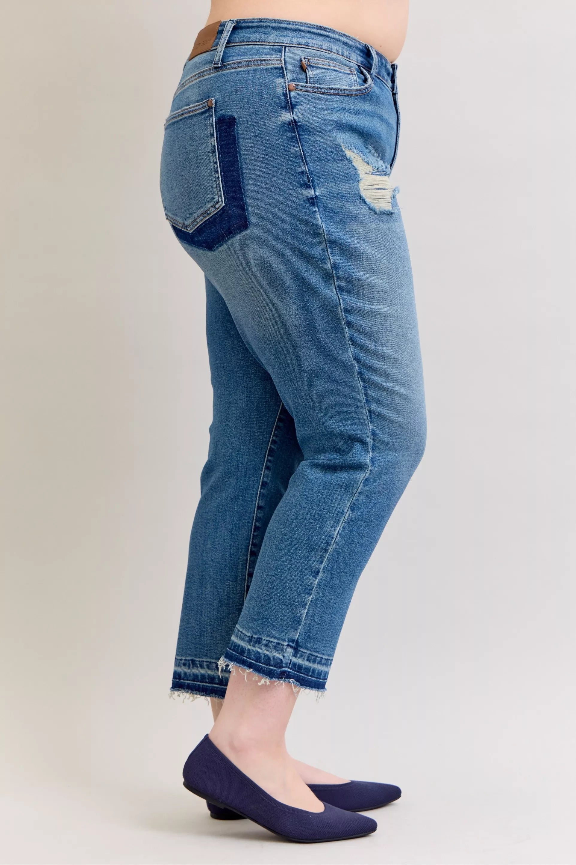 Side view of medium blue mid-rise jeans with stitched repair patches and raw hem