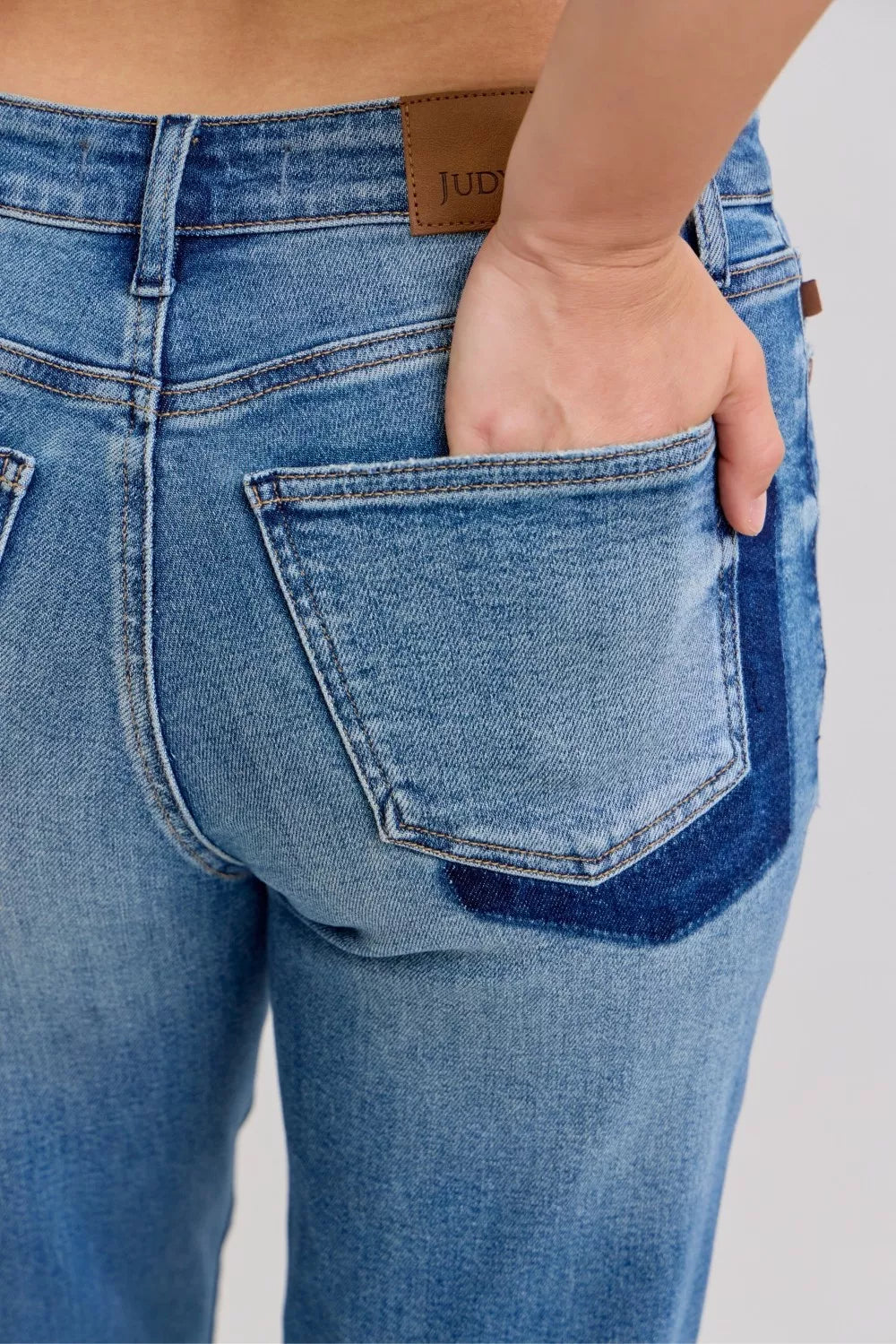 Close-up medium-wash jeans with stitched pocket patch detail and distressed seams