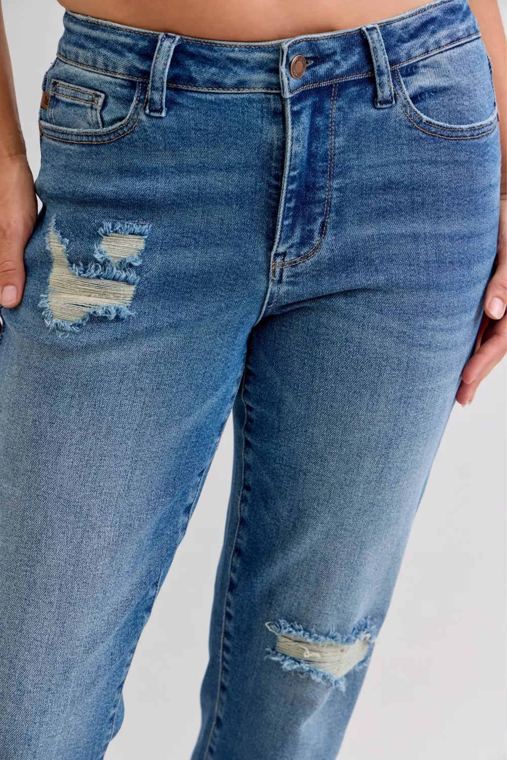Front close-up medium-wash jeans with multiple rips, patch repairs, released hem
