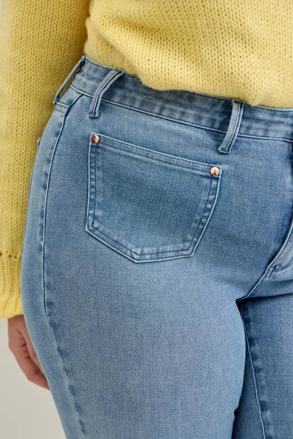 Close-up of light wash jeans front patch pocket, copper buttons, and belt loops
