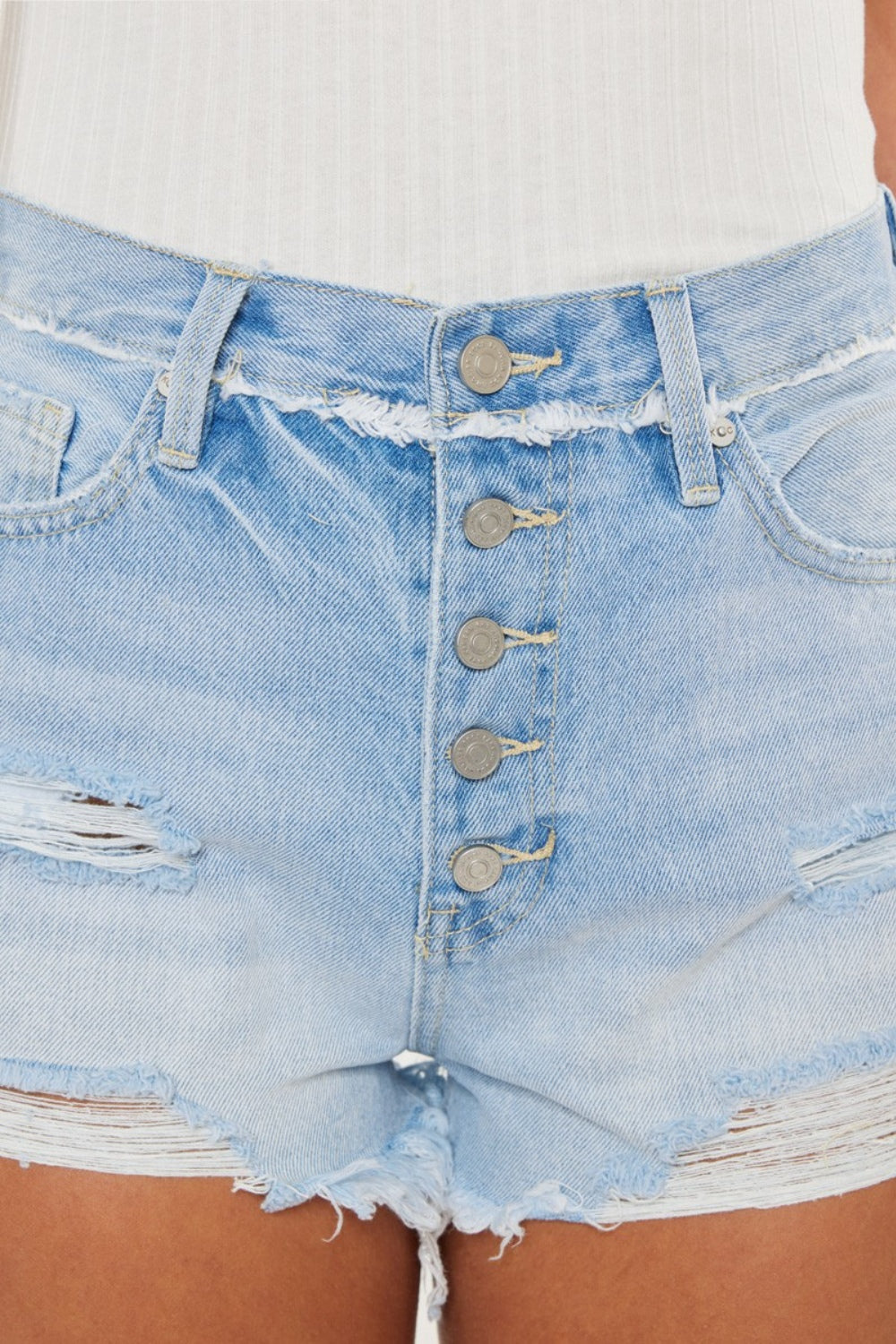 Close-up del frente: bragueta con botones y costuras decorativas en shorts denim azul medio