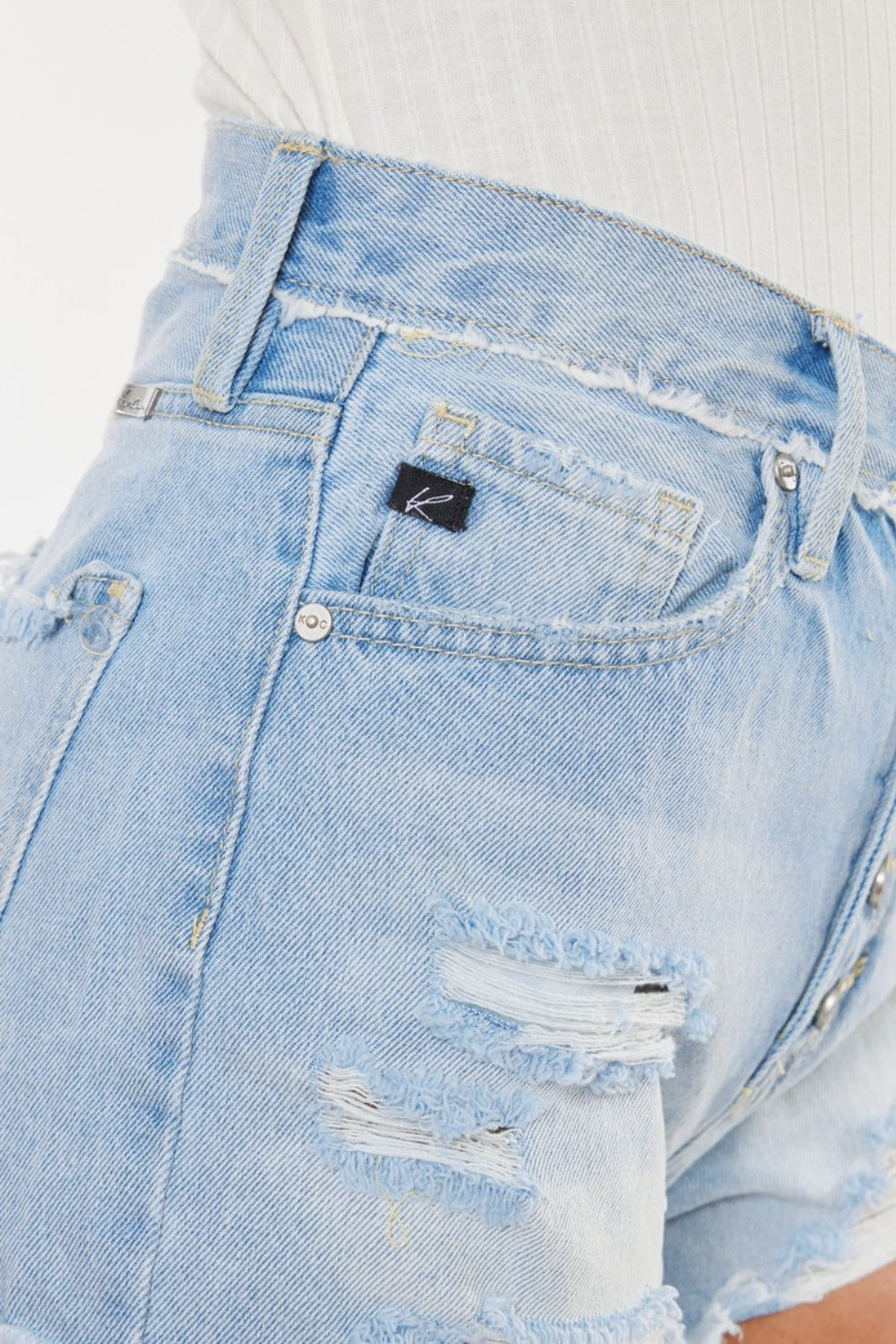 Detalle frontal de shorts denim azul medio: bolsillo trasero desgastado y bragueta con botones