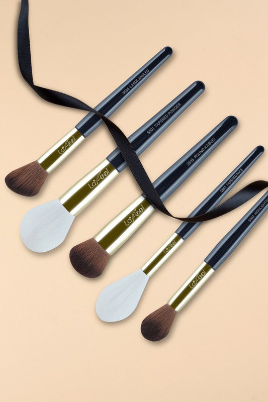 Five makeup brushes with navy handles and ribbon wrap, white and brown bristles
